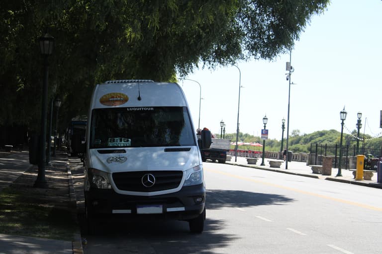 Combi de Luquitour de frente, estacionada en una avenida arbolada