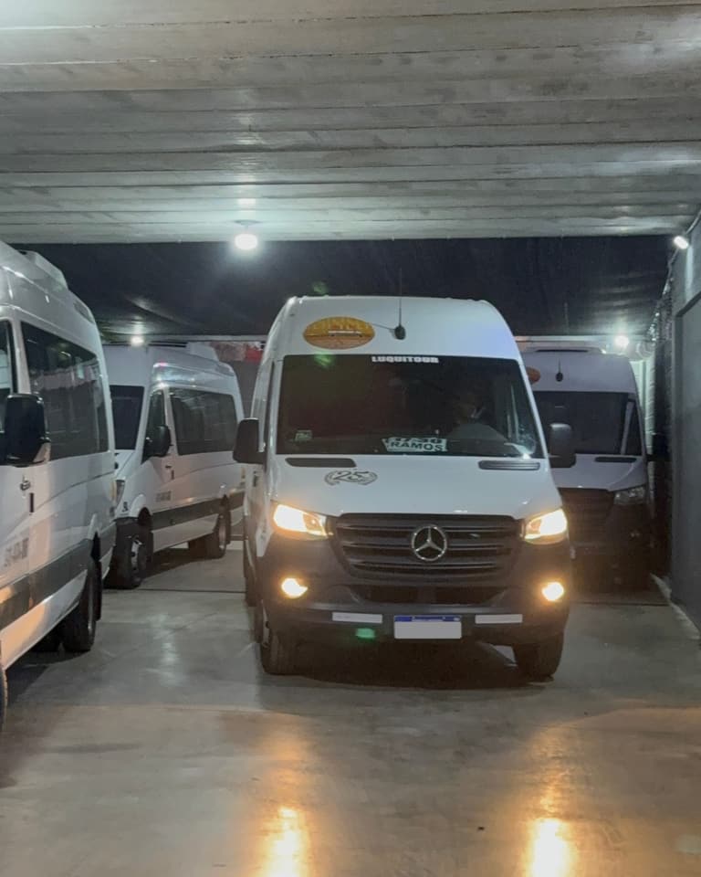 Combi de Luquitour de frente con las luces encendidas, con otras unidades estacionadas en la cochera